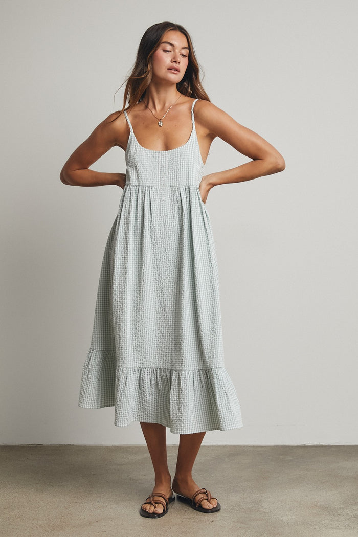 woman wearing a light green gingham midi dress with adjustable straps and a ruffled hem