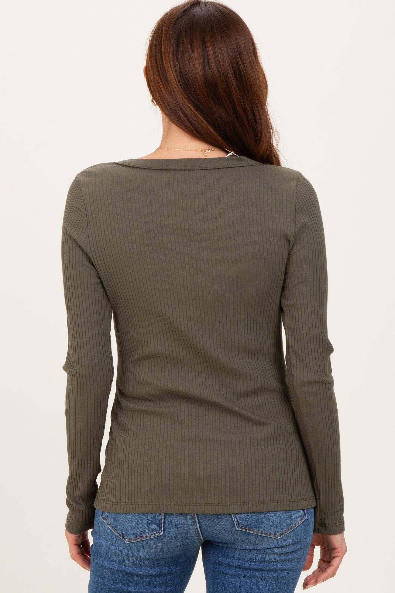 woman wearing an olive green ribbed long sleeve top, seen from the back, paired with blue jeans