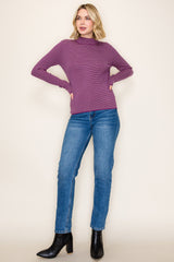 woman wearing a purple and striped long sleeve top with fitted sleeves and blue jeans, paired with black ankle boots
