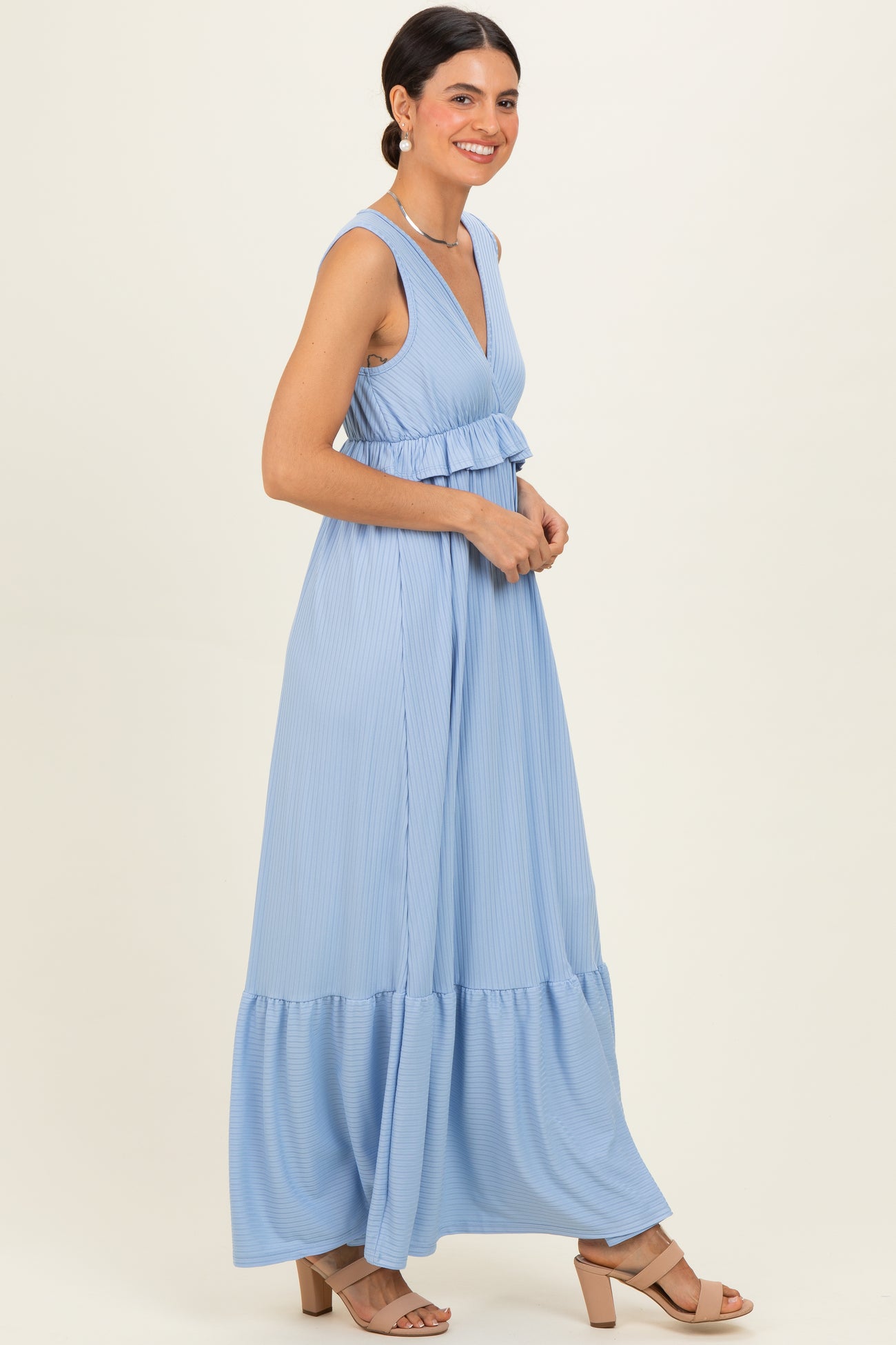 woman wearing a light blue sleeveless maxi dress with a tiered skirt and a fitted bodice, smiling in profile