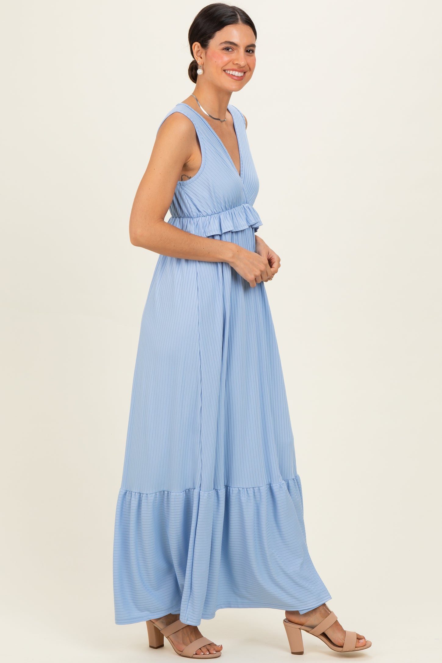 woman wearing a light blue sleeveless maxi dress with a tiered skirt and a fitted bodice, smiling in profile