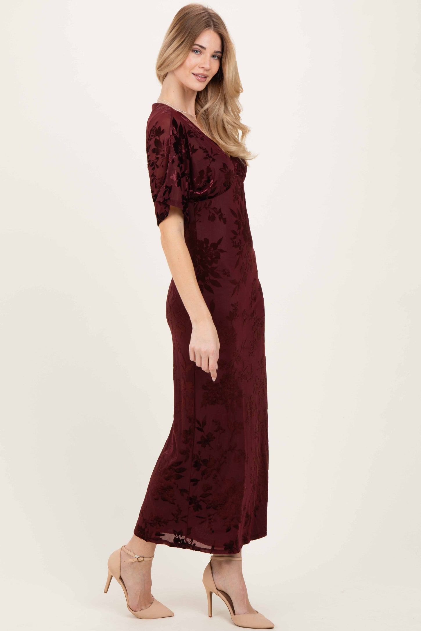 woman wearing a burgundy floral velvet maxi dress with short sleeves and a fitted silhouette