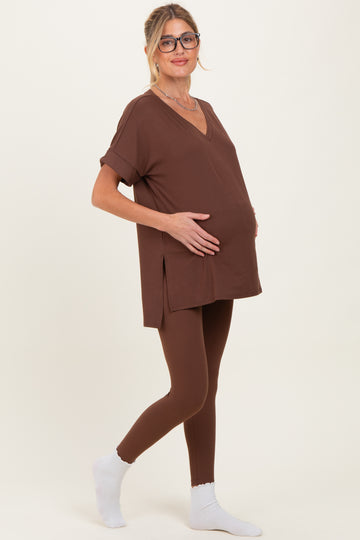 woman wearing a brown maternity top and matching leggings, gently holding her baby bump while standing sideways