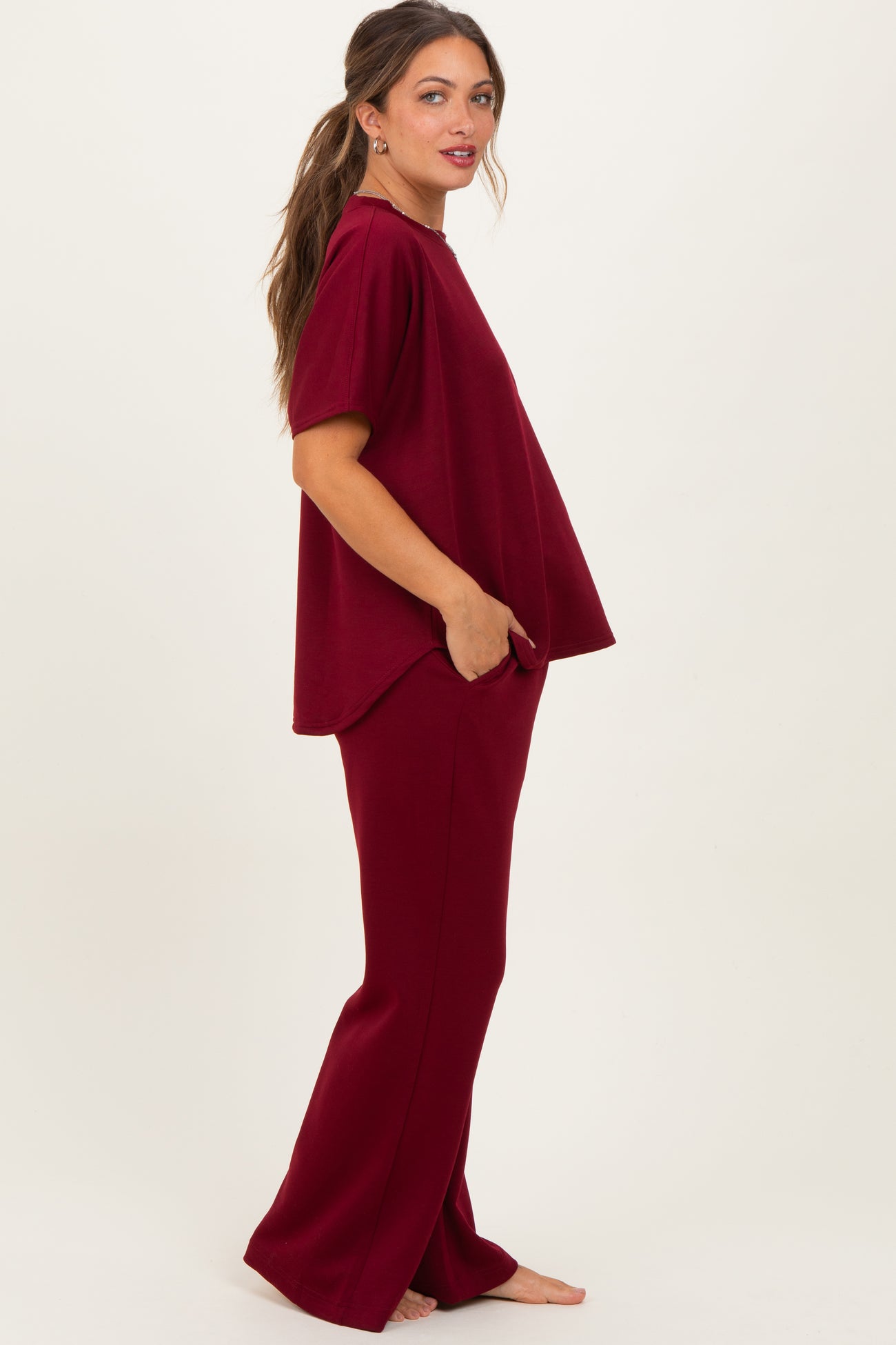 woman wearing a burgundy maternity loungewear set with a loose top and matching pants, baby bump visible