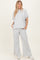 woman wearing a light grey oversized top and matching wide-leg pants, styled casually with white sneakers
