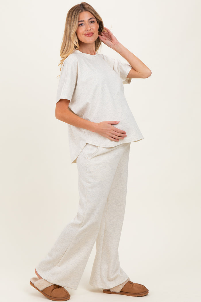woman wearing a light beige maternity loungewear set with a short sleeve top and wide-leg pants, holding her baby bump