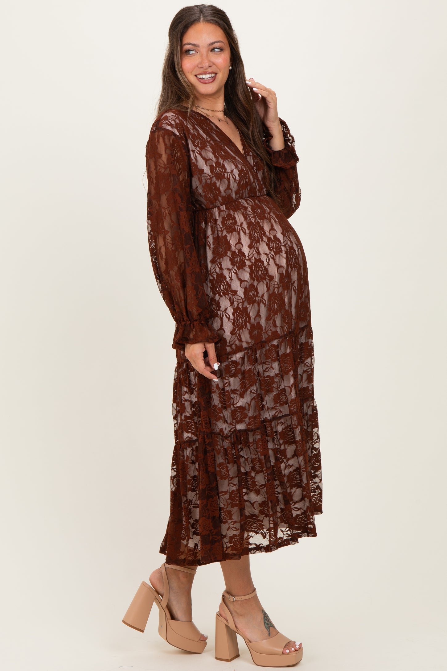 woman wearing a brown lace maternity dress with a tiered skirt and long sleeves, showcasing a visible baby bump