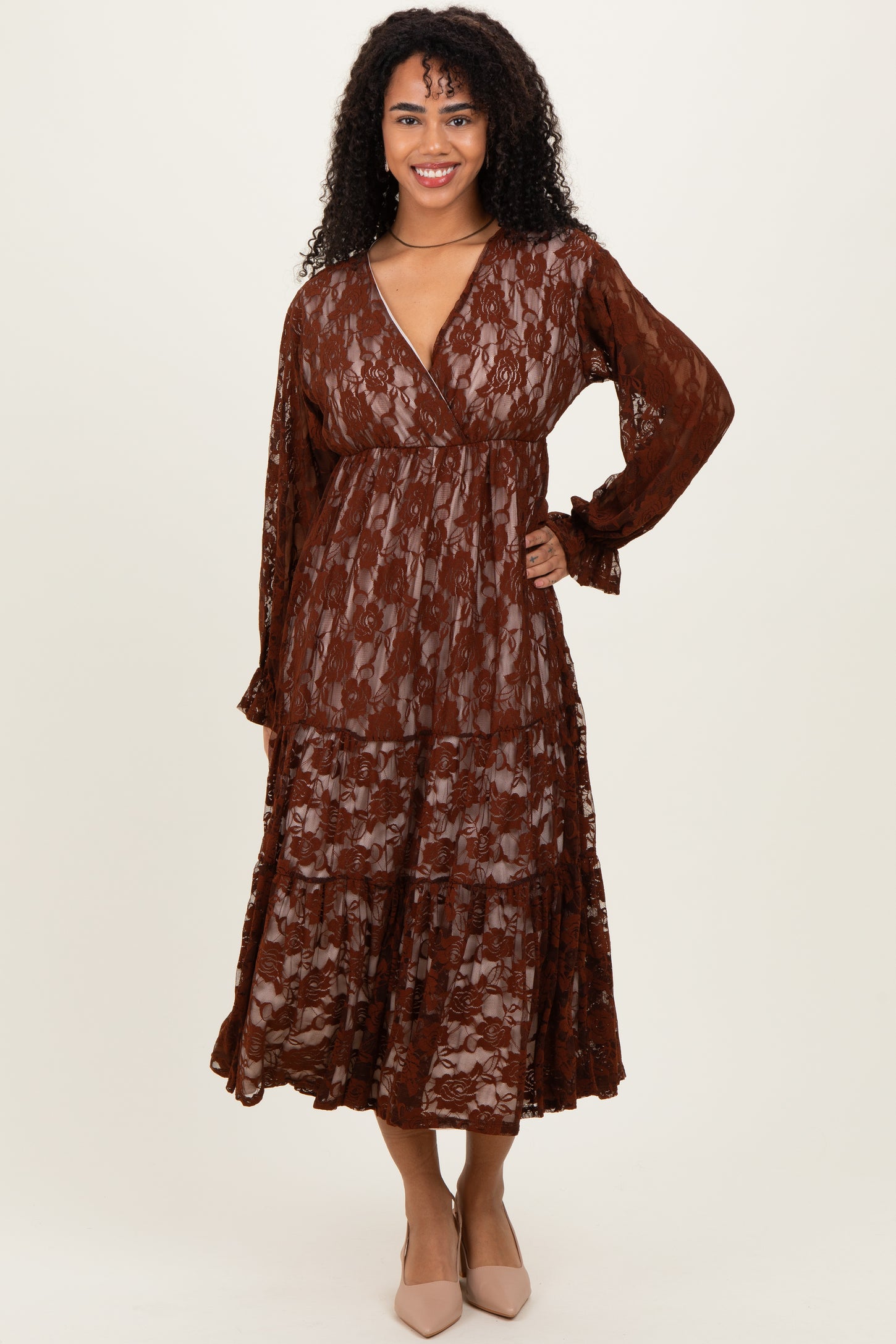 woman wearing a brown lace maxi dress with long sleeves and a tiered skirt, standing and smiling