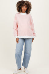 woman wearing a light pink oversized maternity sweatshirt with a white trim and blue jeans, smiling at the camera
