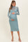 woman wearing a light blue long sleeve maternity dress and holding her baby bump