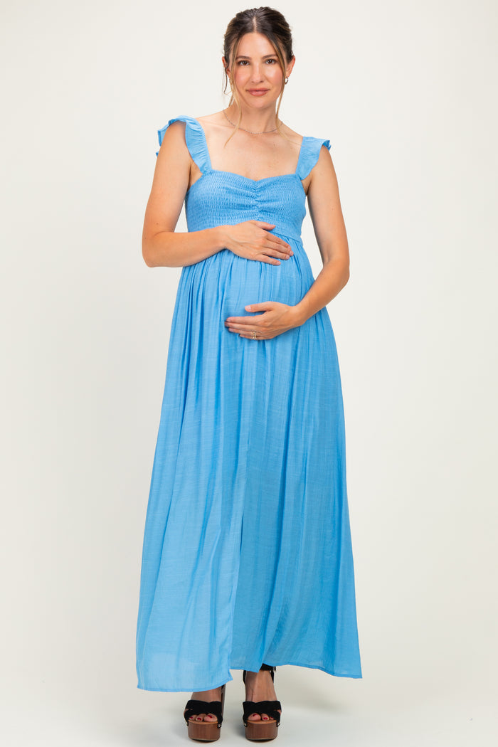 woman wearing a light blue maternity maxi dress with ruffled straps and holding her baby bump