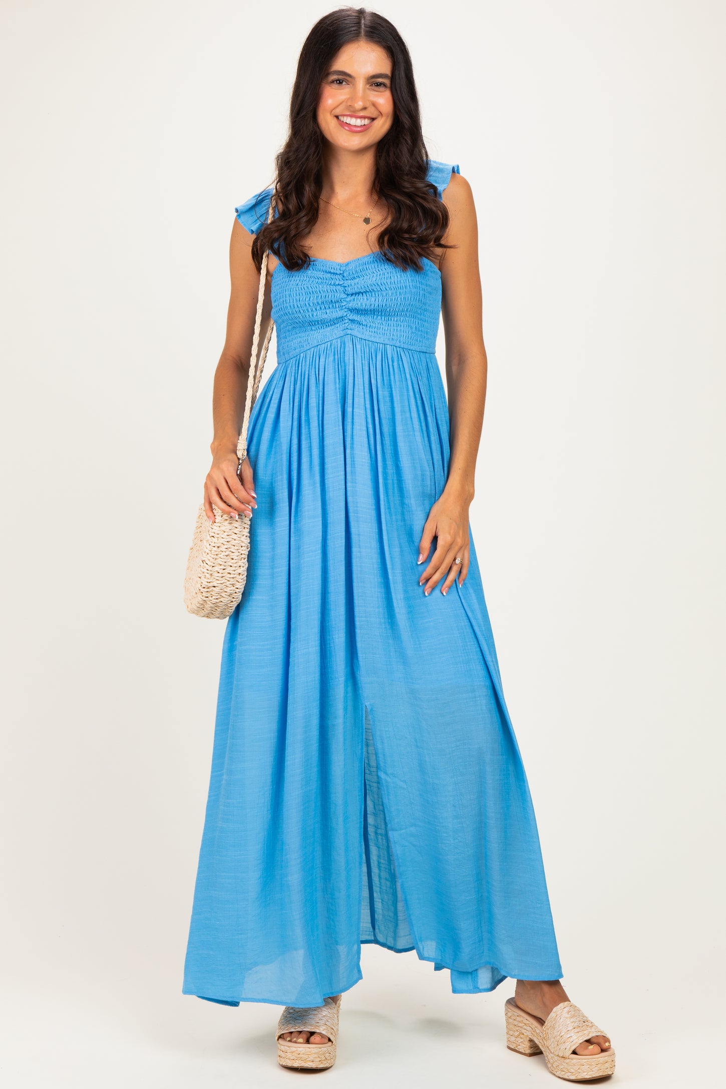 woman wearing a light blue maxi dress with ruffle straps and a smocked bodice, holding a woven bag and wearing platform sandals