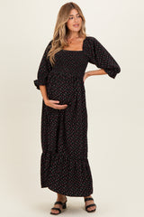 woman wearing a black floral print maternity maxi dress with puff sleeves and holding her baby bump