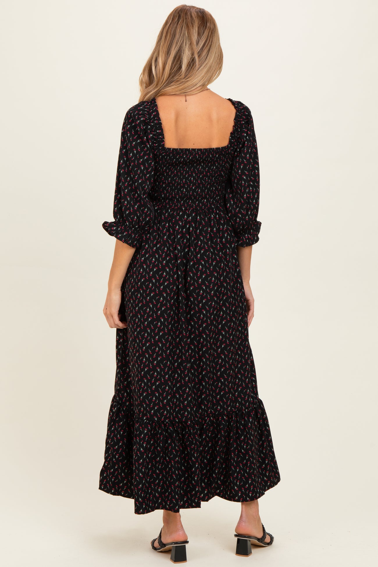 woman wearing a black maternity maxi dress with floral print and puff sleeves, showing a smocked back detail