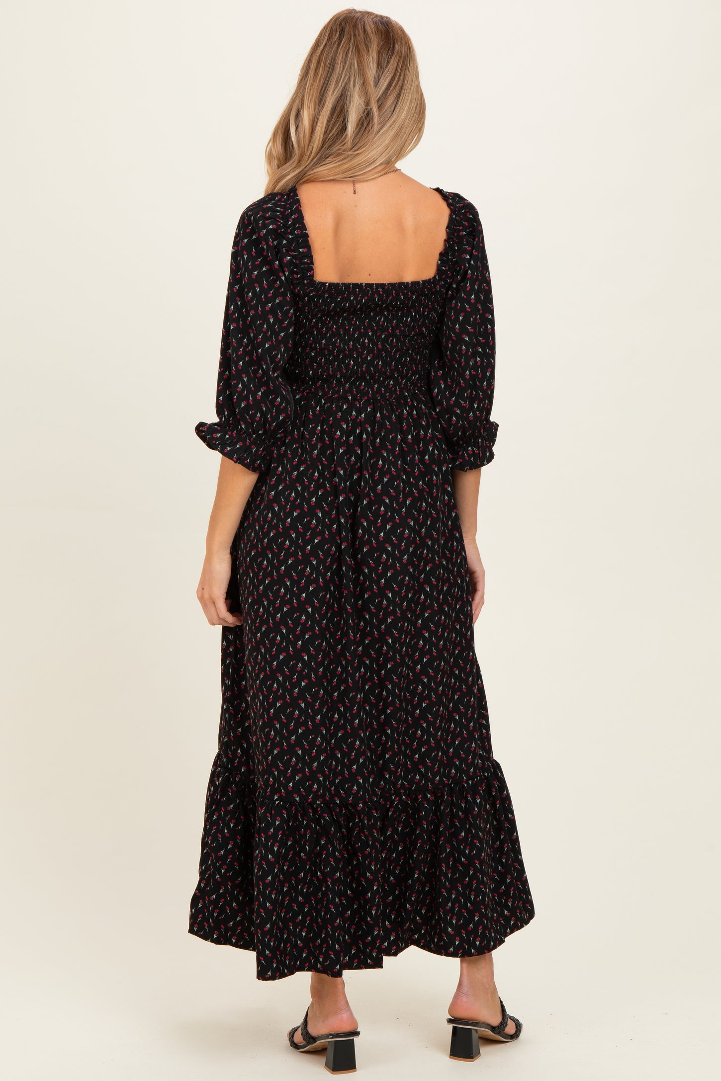 woman wearing a black maternity maxi dress with floral print and puff sleeves, showing a smocked back detail