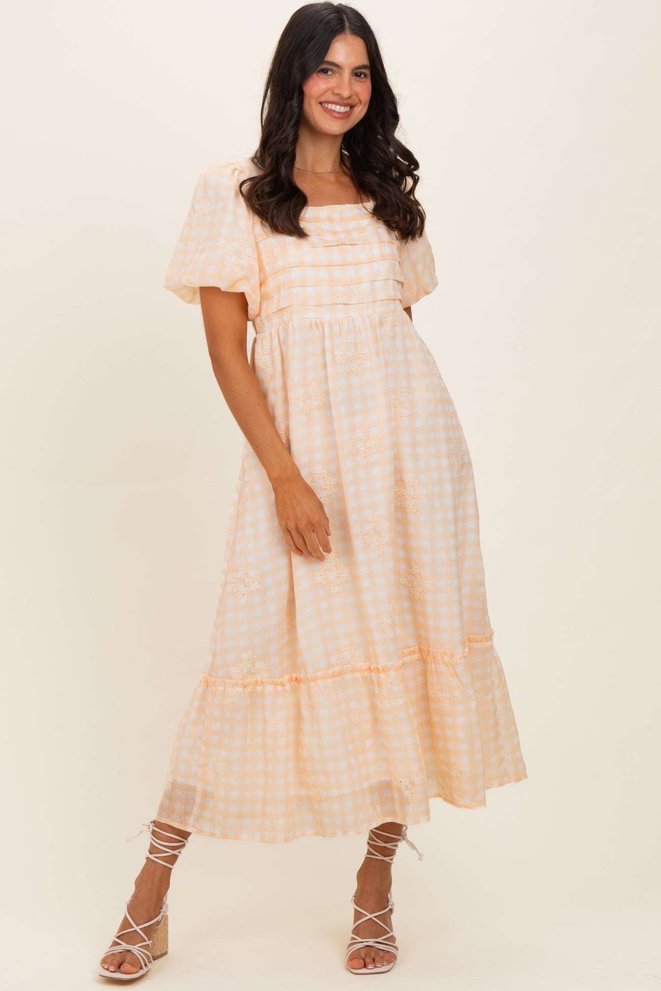 woman wearing a light orange gingham print maxi dress with short puff sleeves and a tiered hemline