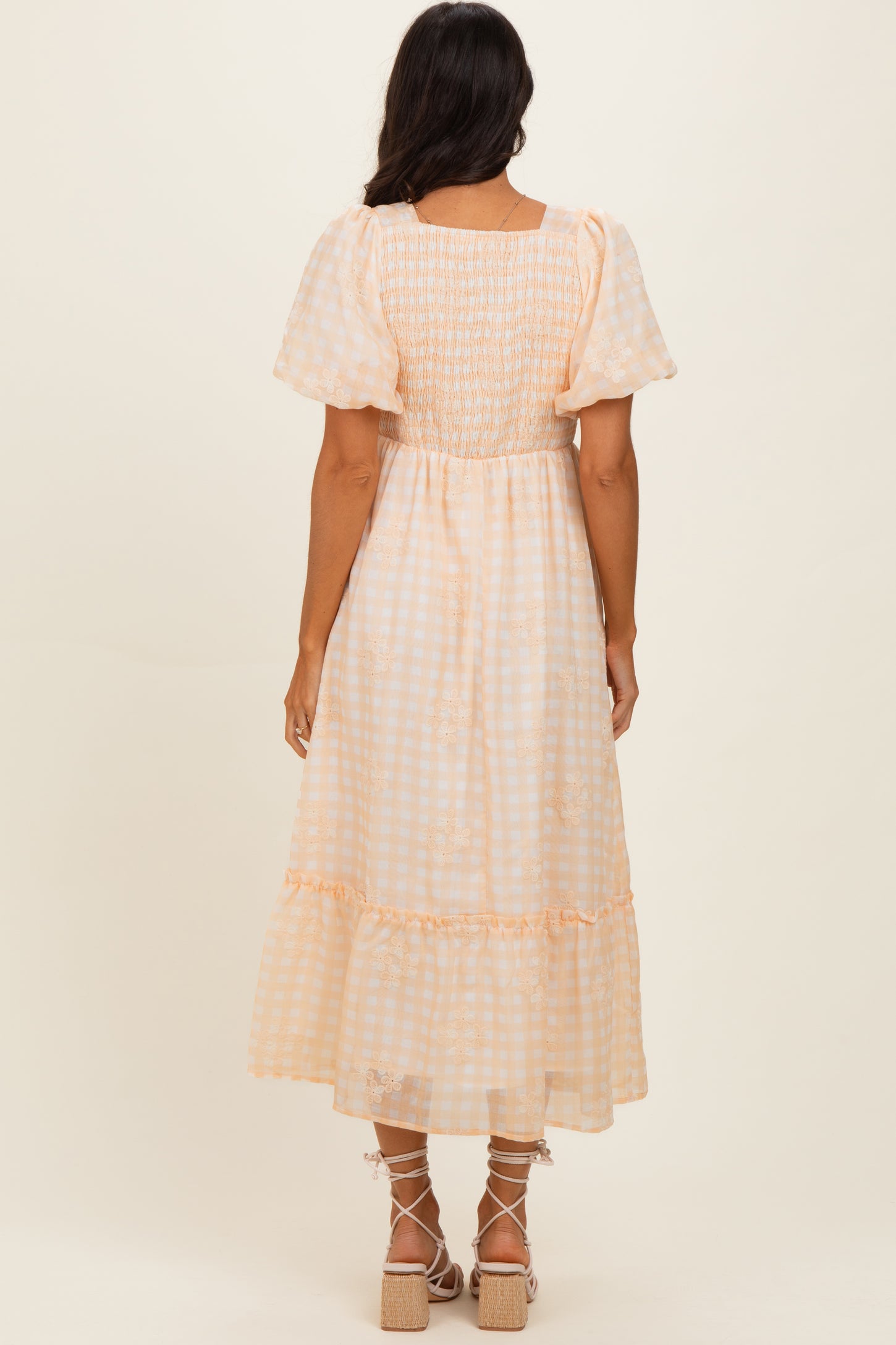 woman wearing a light orange and white gingham smocked maxi dress with puff sleeves and ruffle hem