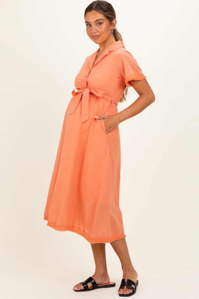 woman wearing an orange maternity dress with a tied waist and pockets, featuring short sleeves and a flared skirt, showing baby bump