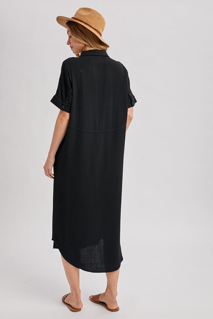 woman wearing a black oversized shirt dress with rolled sleeves and a straw hat, viewed from the back