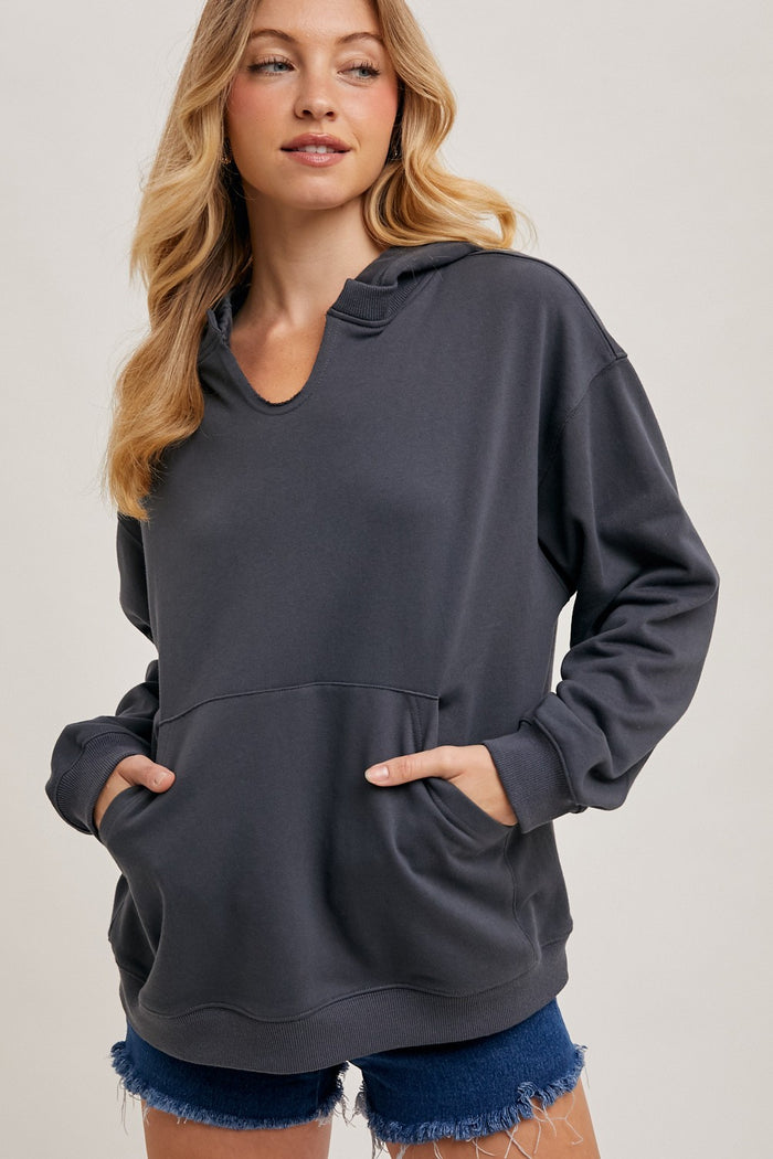 woman wearing a dark gray hooded sweatshirt with a front pocket and a relaxed fit paired with denim shorts