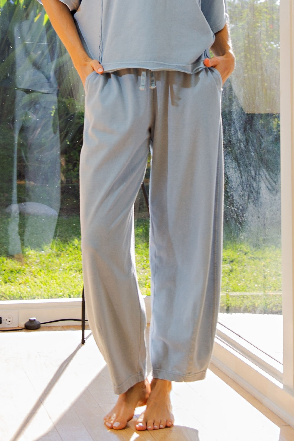 woman wearing light blue wide-leg lounge pants with an elastic waistband and drawstring, standing barefoot indoors