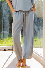 woman wearing light blue wide-leg lounge pants with an elastic waistband and drawstring, standing barefoot indoors