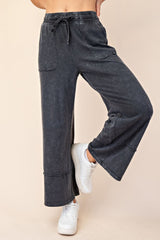woman wearing dark grey wide-leg sweatpants with pockets and drawstring waistband, styled with white sneakers