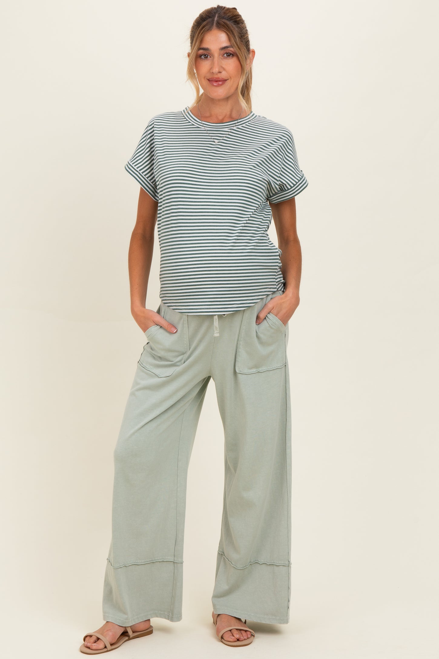 woman wearing a striped maternity top and light green wide-leg maternity pants with pockets, posing with a baby bump visible