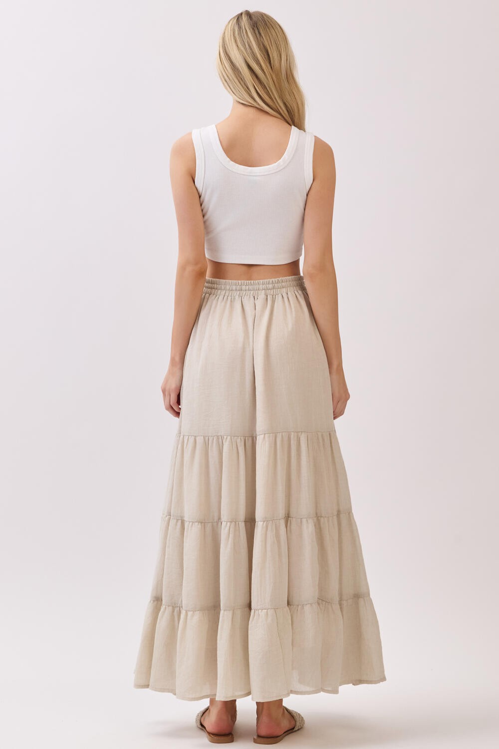 woman wearing a white cropped tank top and a long beige tiered maxi skirt, seen from the back