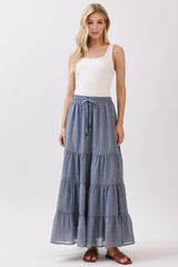 woman wearing a white tank top and a long tiered blue maxi skirt with an elastic waistband and drawstring