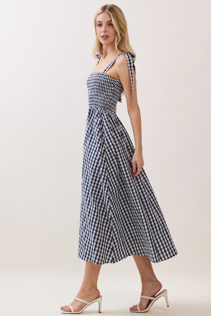 woman wearing a navy and white gingham midi dress with tie straps and a fitted bodice