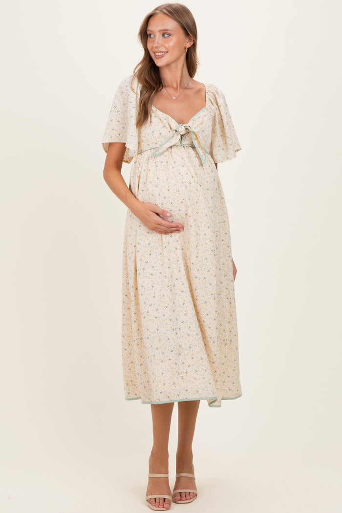 woman wearing a floral print maternity dress with a tie front, short flutter sleeves, and showing her baby bump