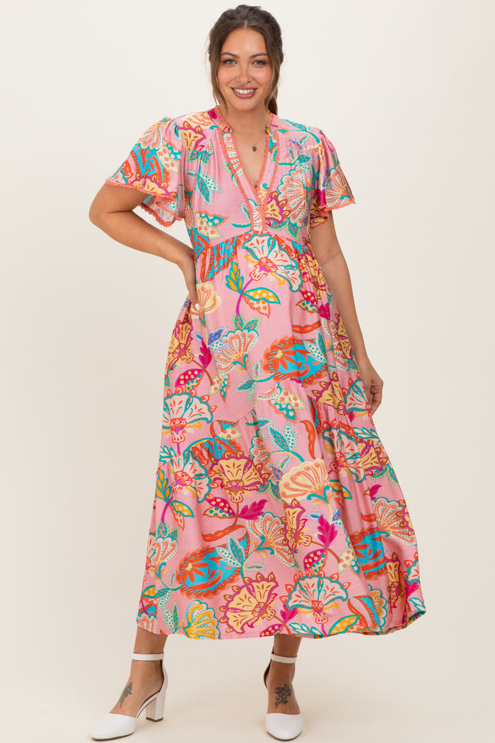 woman wearing a pink floral maternity maxi dress with short sleeves and a v-neckline, smiling while posing