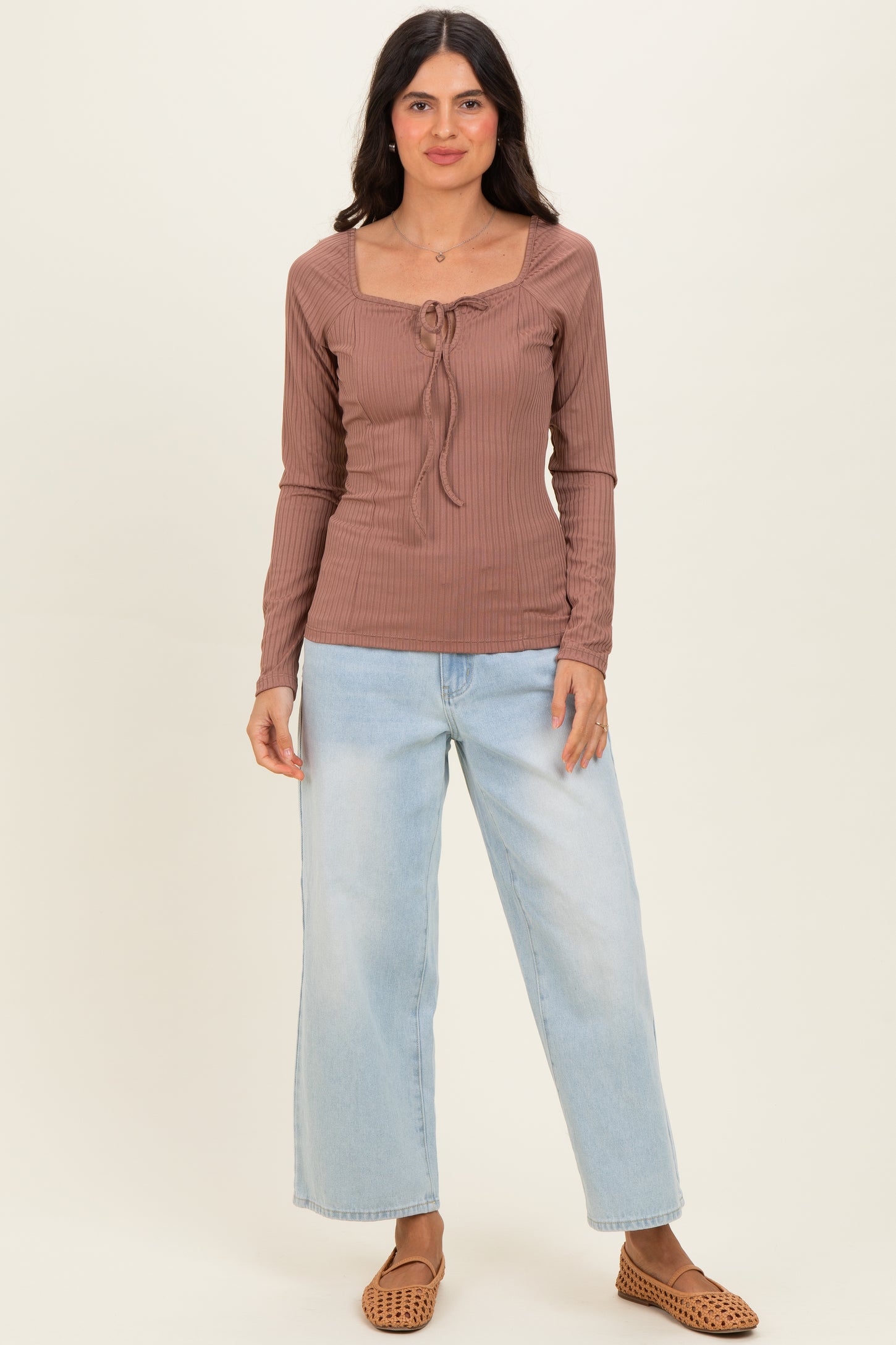 woman wearing a brown ribbed long sleeve top with a square neckline and tie detail, paired with light blue wide-leg jeans