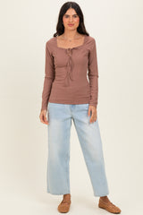 woman wearing a brown ribbed long sleeve top with a square neckline and tie detail, paired with light blue wide-leg jeans