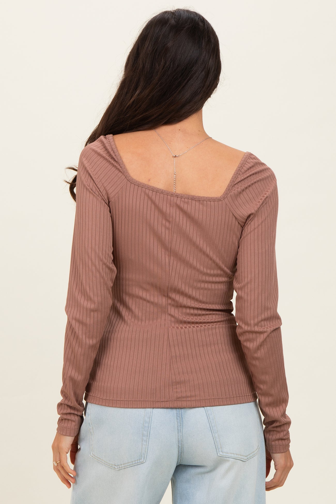 woman wearing a mauve ribbed long sleeve top with a square neck and gathered shoulder details, viewed from the back