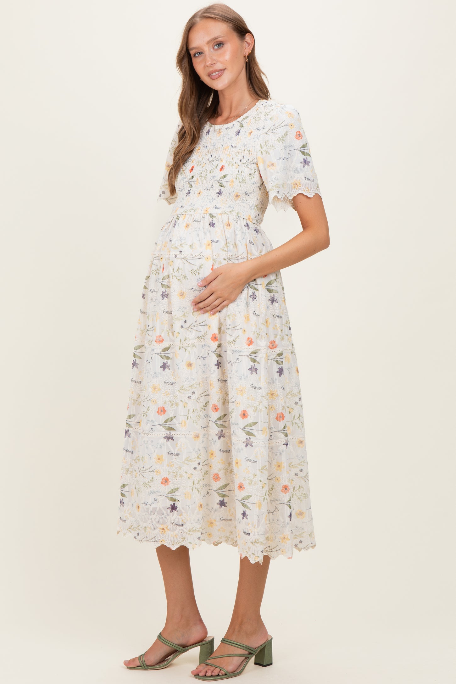 woman wearing a floral print maternity dress with short sleeves and smocked bodice, holding her baby bump