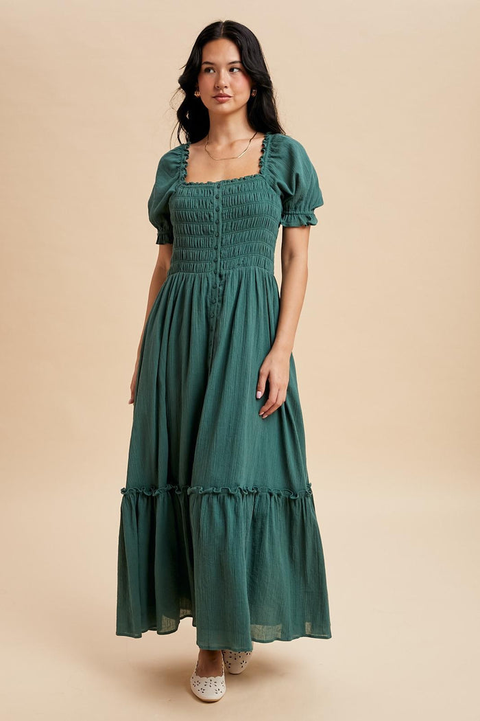woman wearing a green maxi dress with puff sleeves and a tiered hem, standing against a beige background