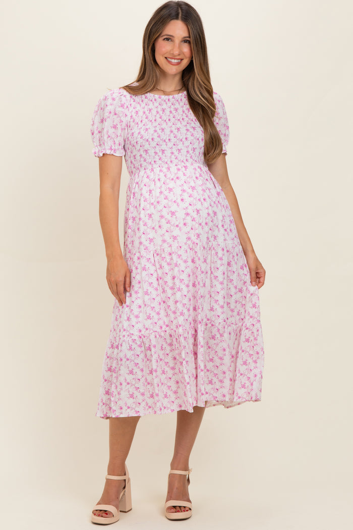 woman wearing a pink floral maternity dress with puff sleeves and a tiered skirt, showcasing a baby bump