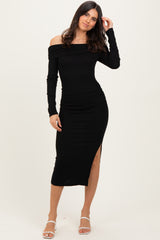 woman wearing a black off-shoulder midi dress with long sleeves and side slit, standing and touching her hair