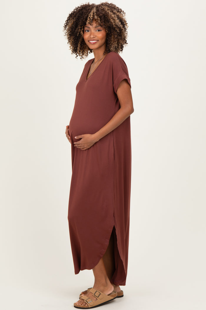 woman wearing a rust colored maternity maxi dress with a side slit and holding her baby bump