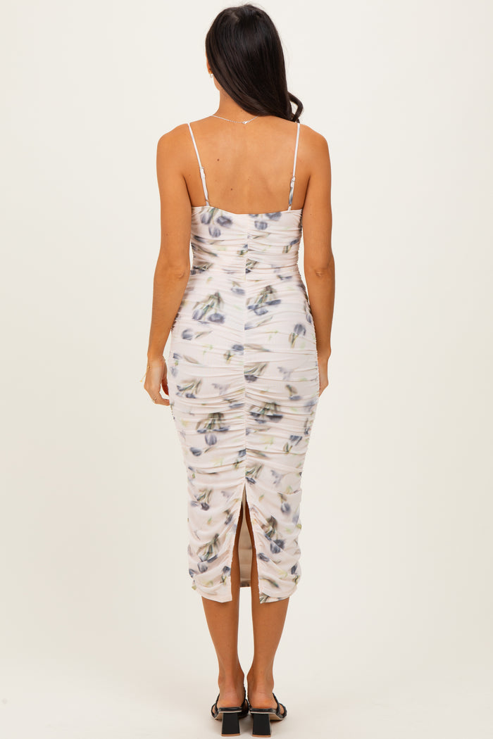 woman wearing a fitted floral midi dress with ruching and a back slit, showing the back view