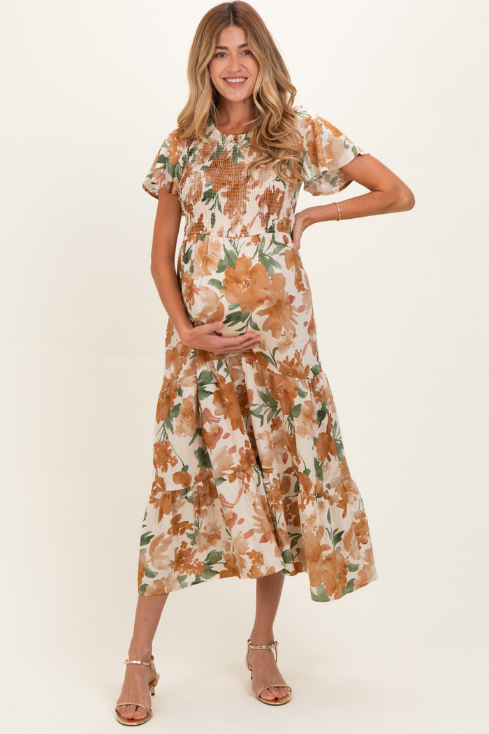 woman wearing a floral maternity dress with short sleeves and a tiered skirt, gently cradling her baby bump