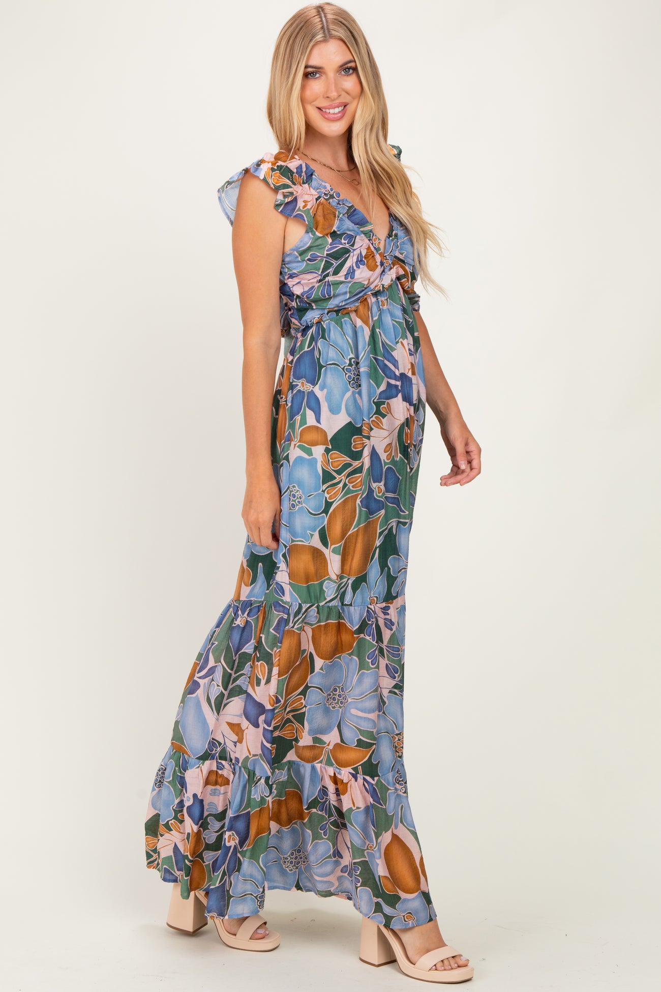 woman wearing a floral maxi dress in blue, orange, and green with ruffle sleeves and a tie front detail