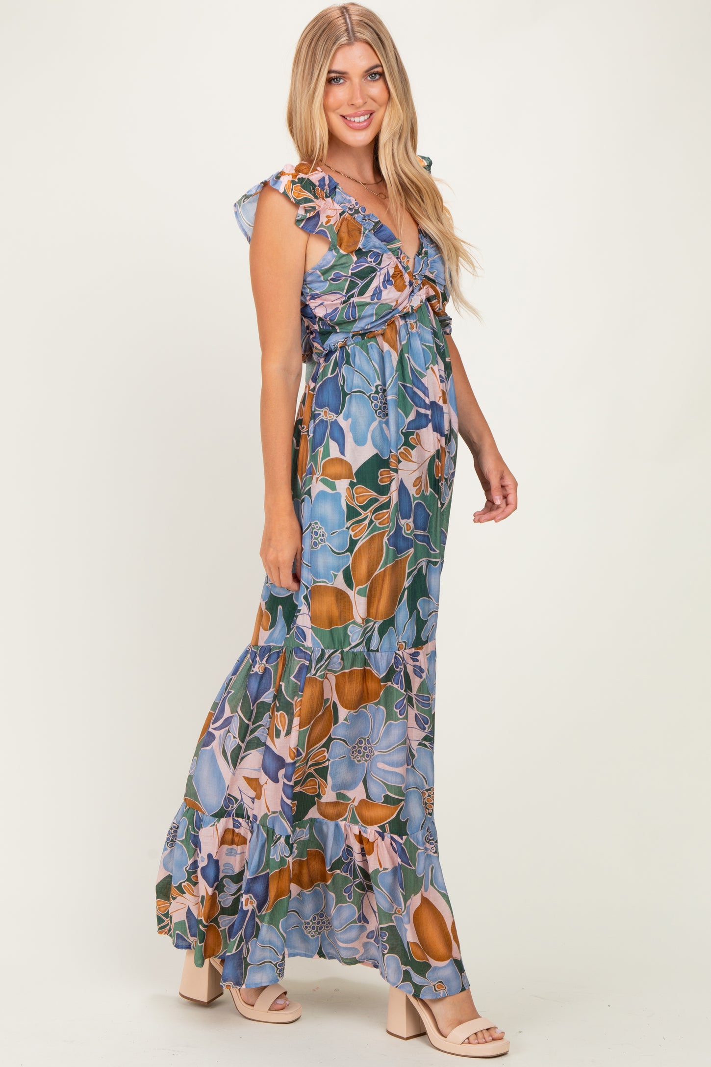 woman wearing a floral maxi dress in blue, orange, and green with ruffle sleeves and a tie front detail
