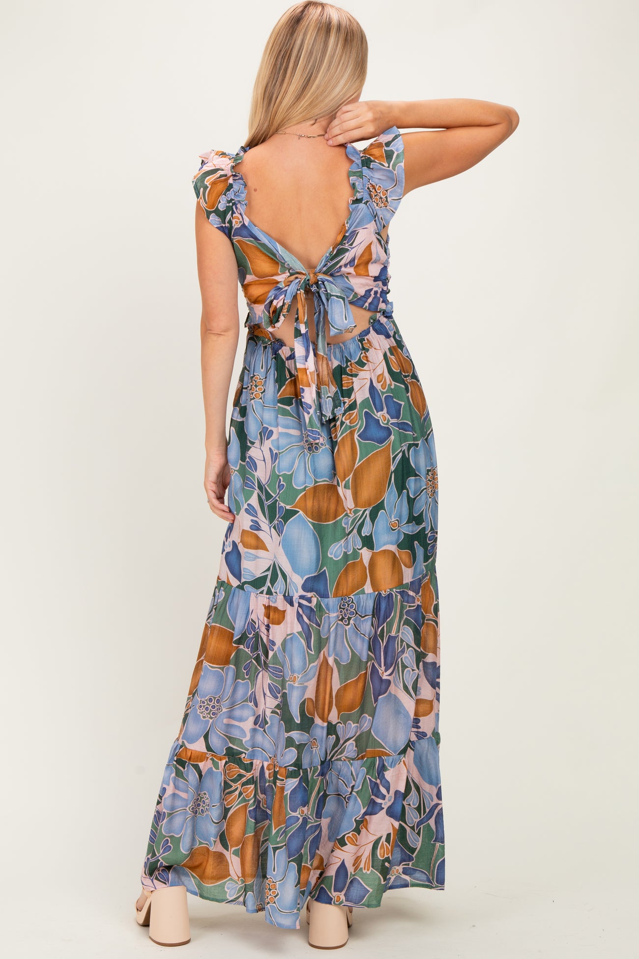 woman wearing a floral maxi dress with ruffle sleeves and an open back tied with a bow