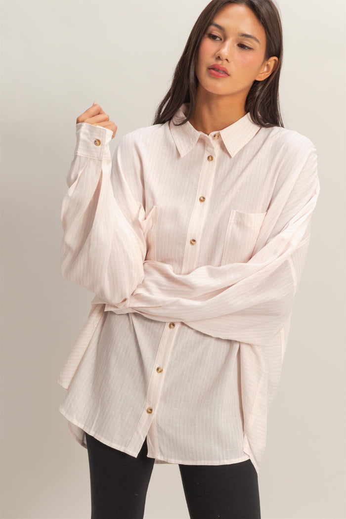 woman wearing a light pink oversized button-up shirt with a front pocket and long sleeves, styled with black leggings