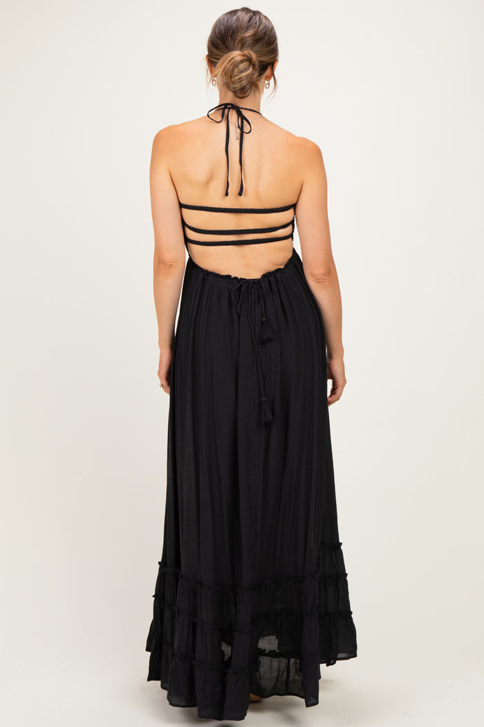 woman wearing a black halter neck maternity maxi dress with adjustable straps and ruffle details, showcasing a baby bump