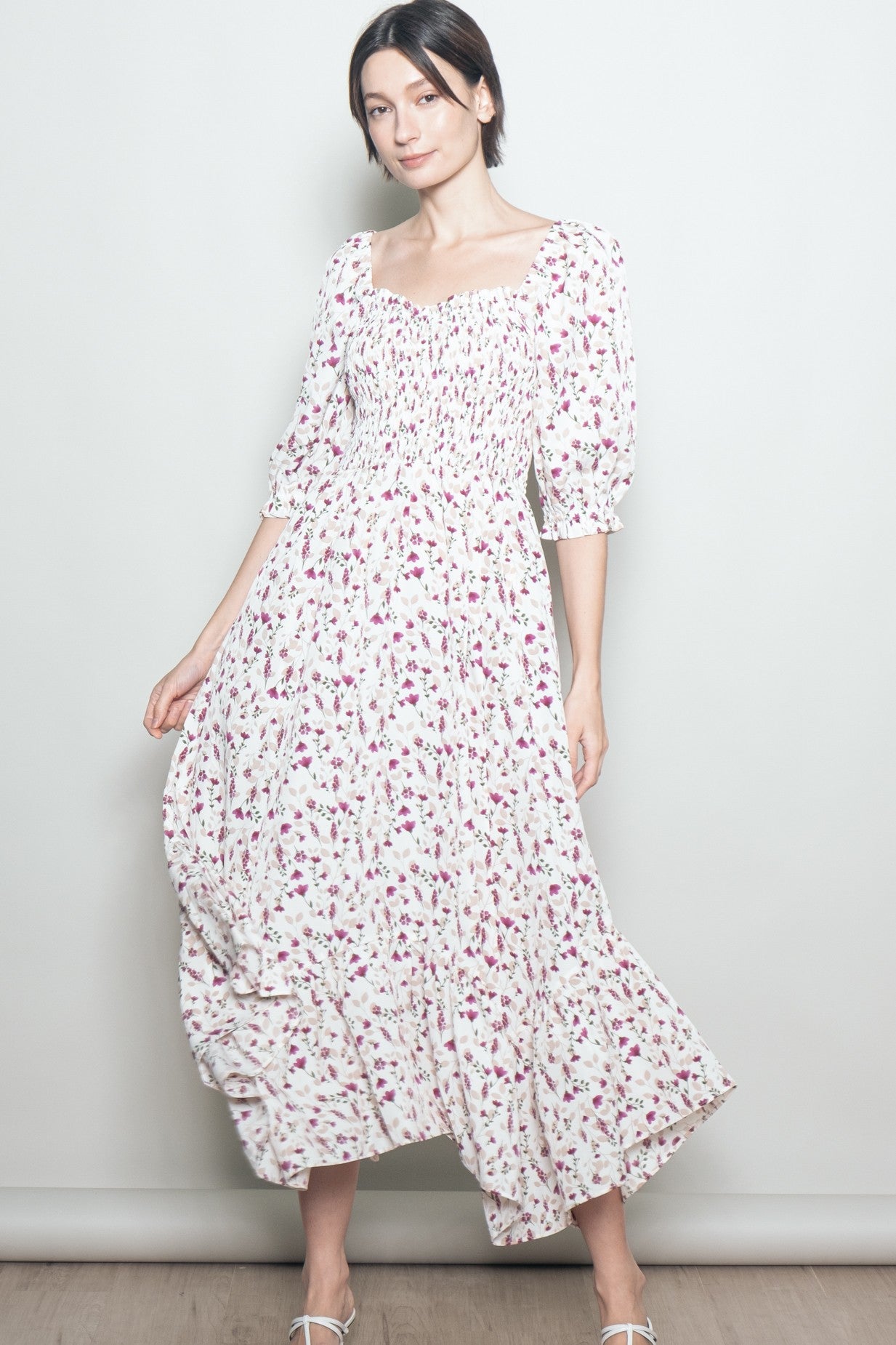 woman wearing a white floral maxi dress with smocked bodice and puff sleeves, standing against a plain background