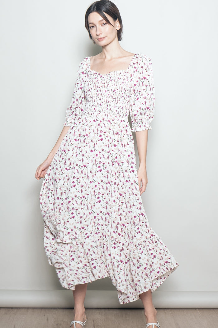 woman wearing a white floral maxi dress with smocked bodice and puff sleeves, standing against a plain background
